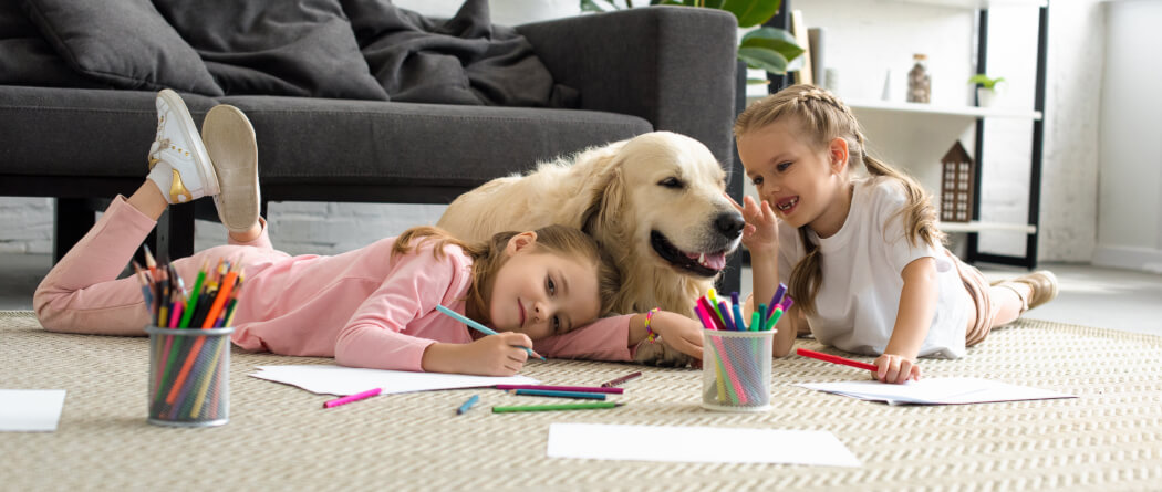 Two kids on the floor coloring with a dog